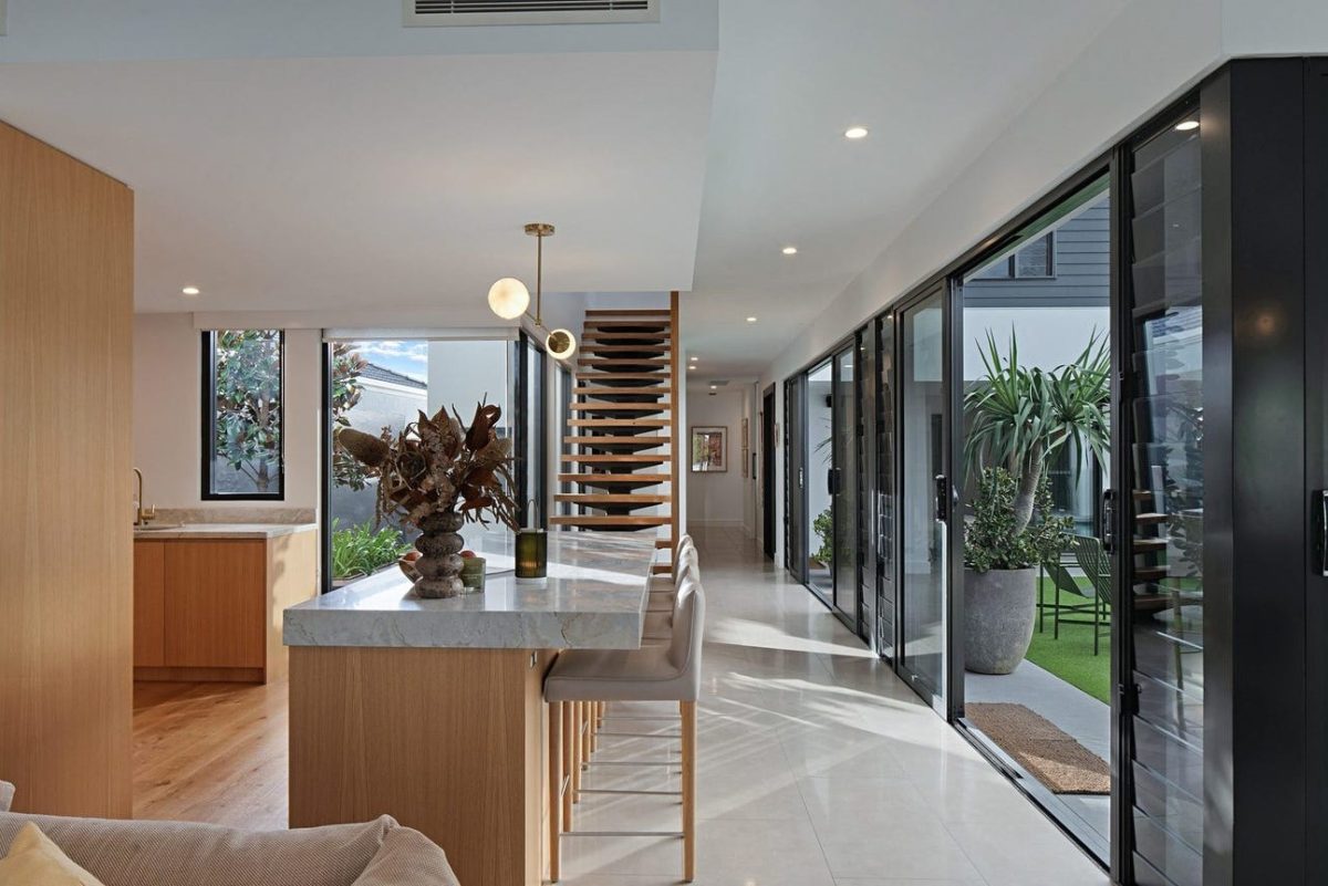 Hallway view at 28 Kookaburra Court, Sorrento, showing the kitchen island bench, timber tread staircase, and courtyard through sliding doors