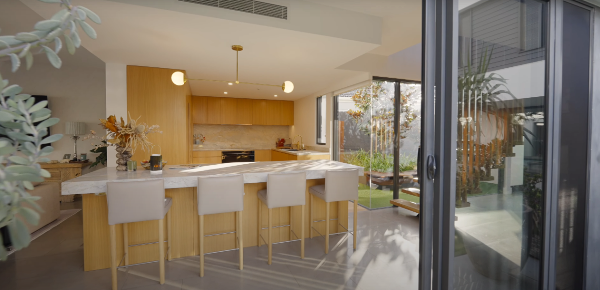 Kitchen courtyard and kitchen at 28 Kookaburra Court, Sorrento, viewed from the main courtyard, featuring a floor to ceiling corner glass window, outdoor timber seating, and a magnolia tree